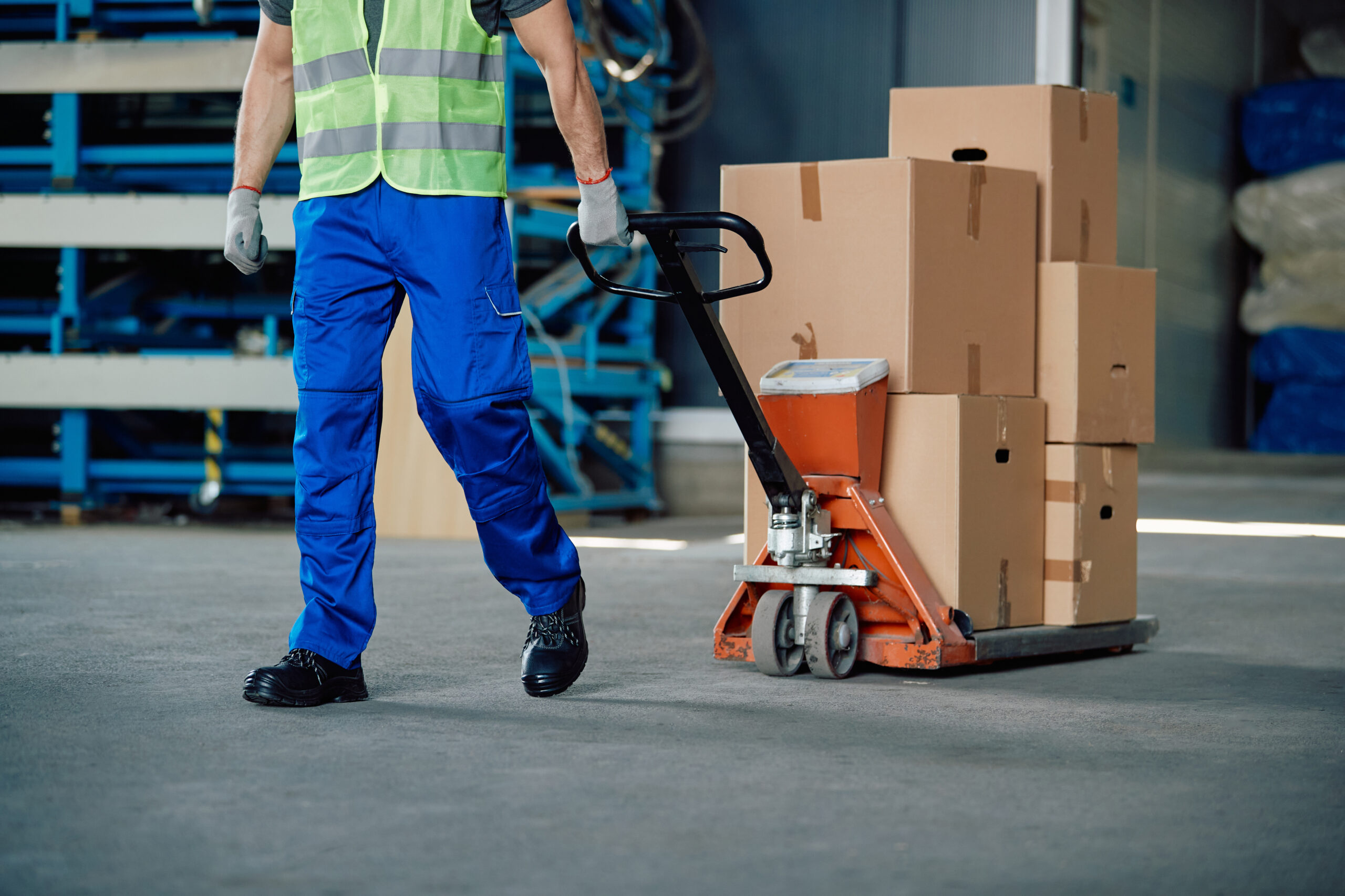 Unrecognizable worker pulls pallet jack while working at distribution warehouse.